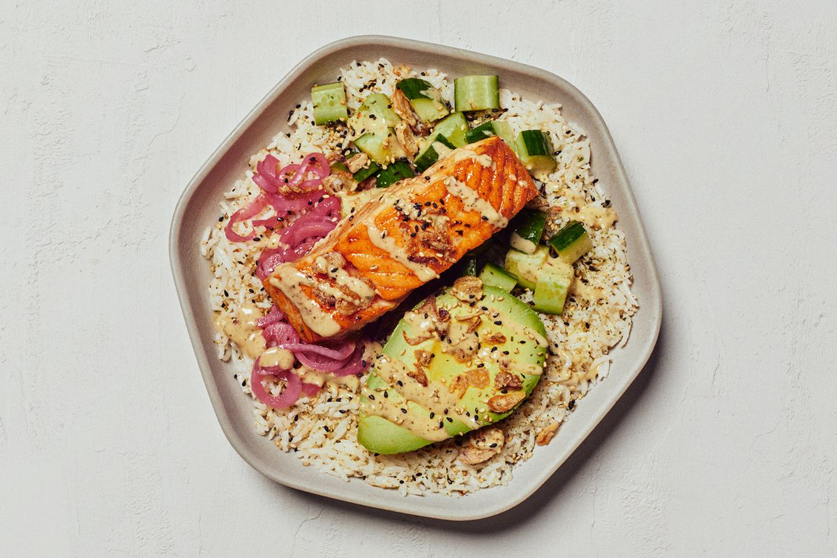 A hexagonal plate of a filet of salmon and an avocado, served on rice and drizzled with sauce