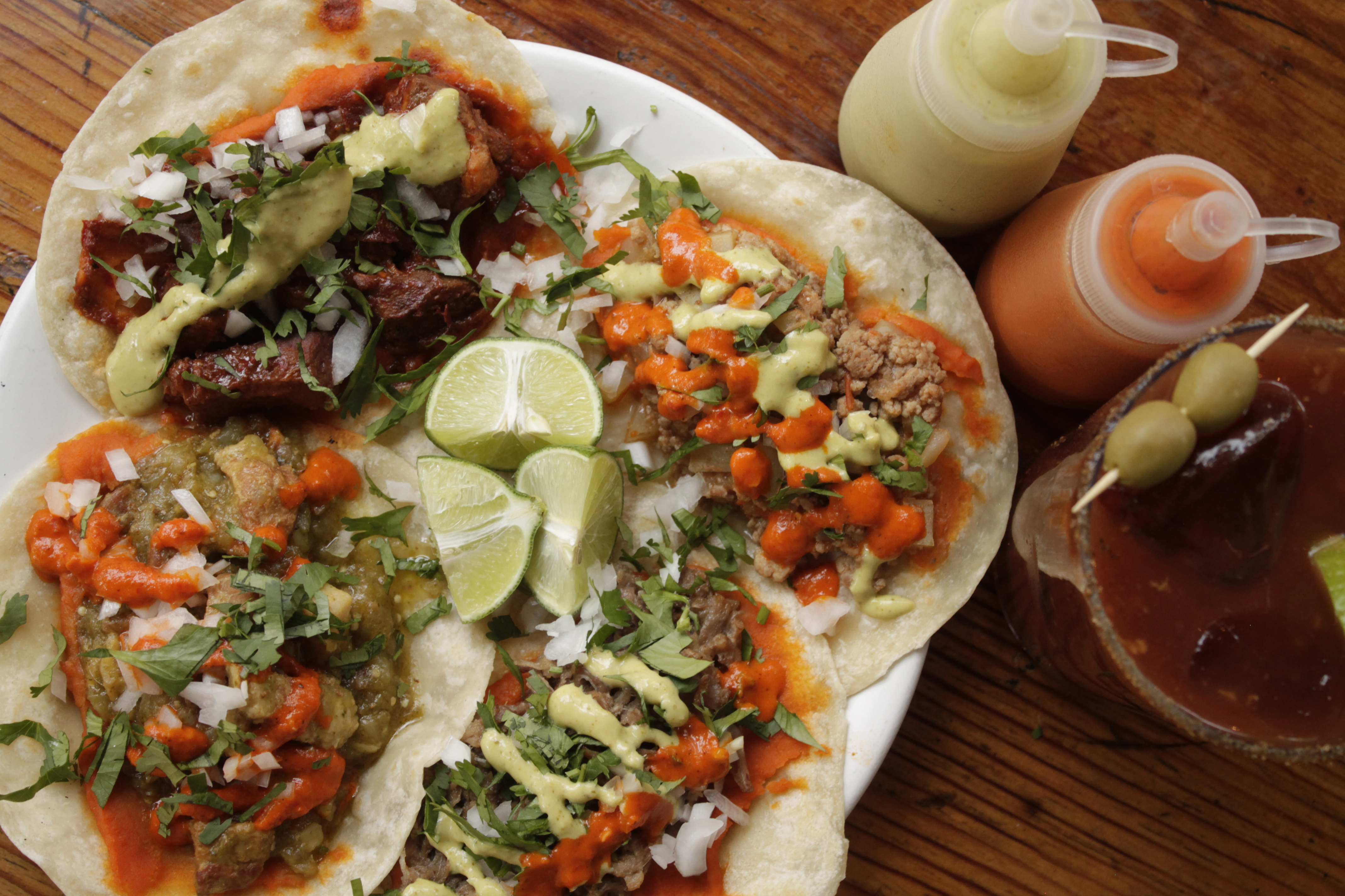 Four overloaded tacos, with lime wedges and squeeze bottles of sauces.